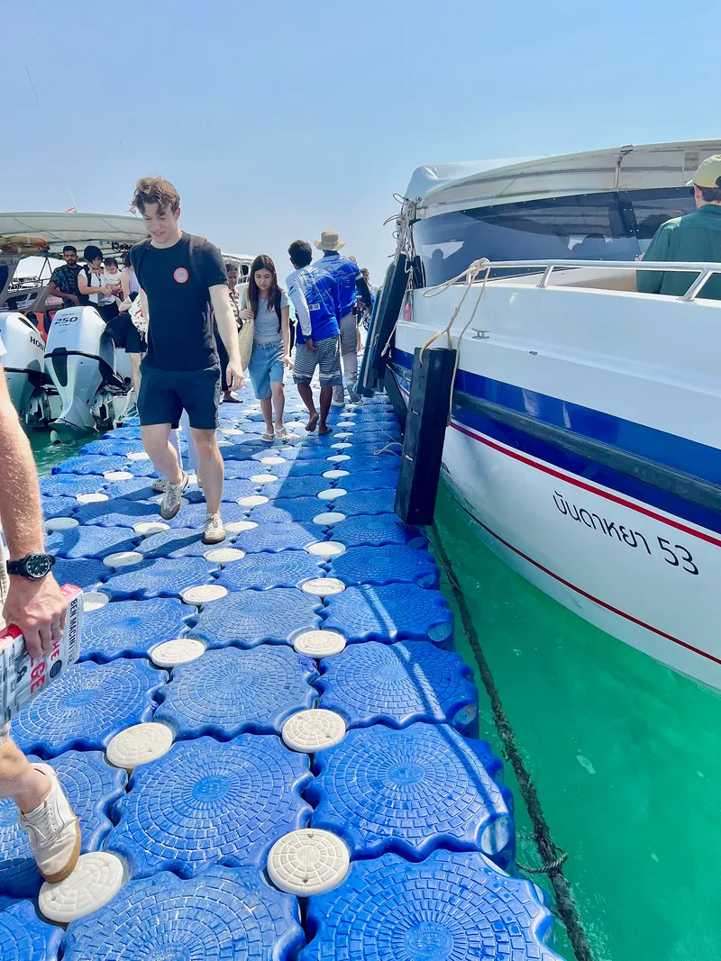 Passengers walking along a floating pontoon from a speedboat to the beach