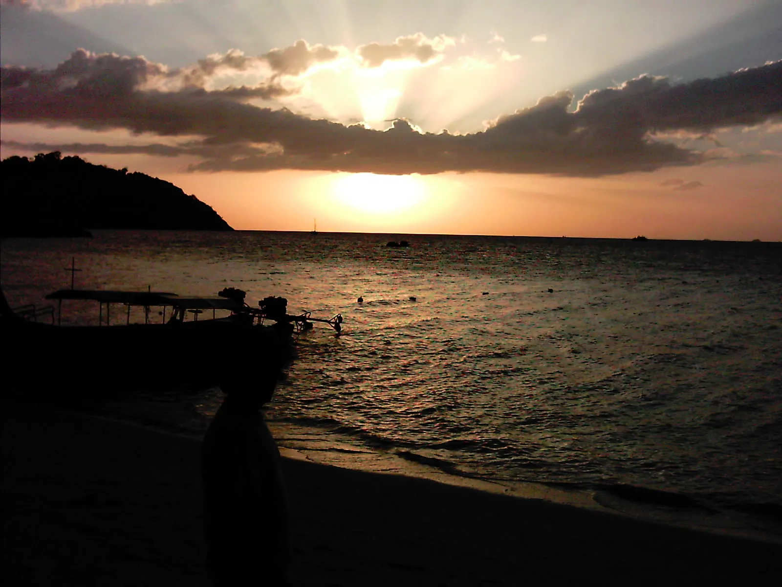 Sunset over the sea from a Koh Lipe beach, a longtail boat in silhouette