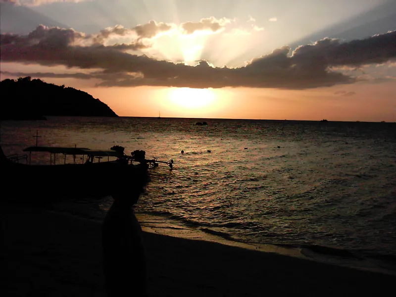 Sunset over the sea from a Koh Lipe beach, a longtail boat in silhouette