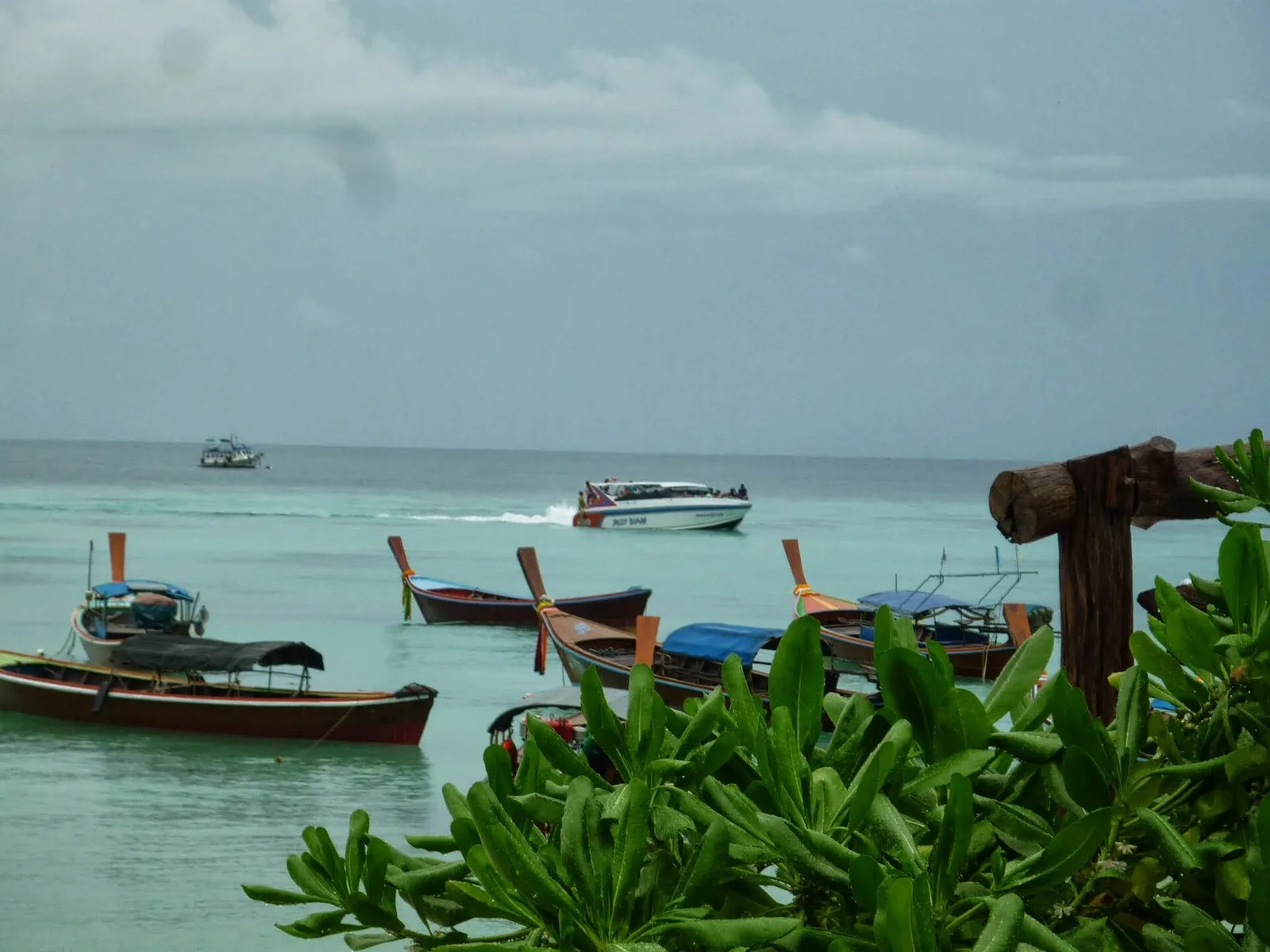 Longtail boats and a speedboat off a Koh Lipe beach under grey cloud