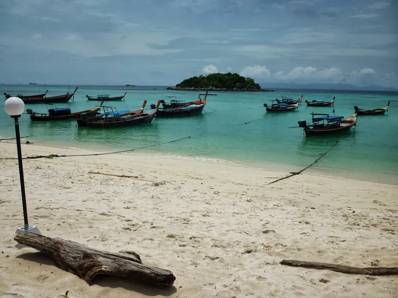 Longtail boats moored off a Koh Lipe beach, a small wooded islet behind